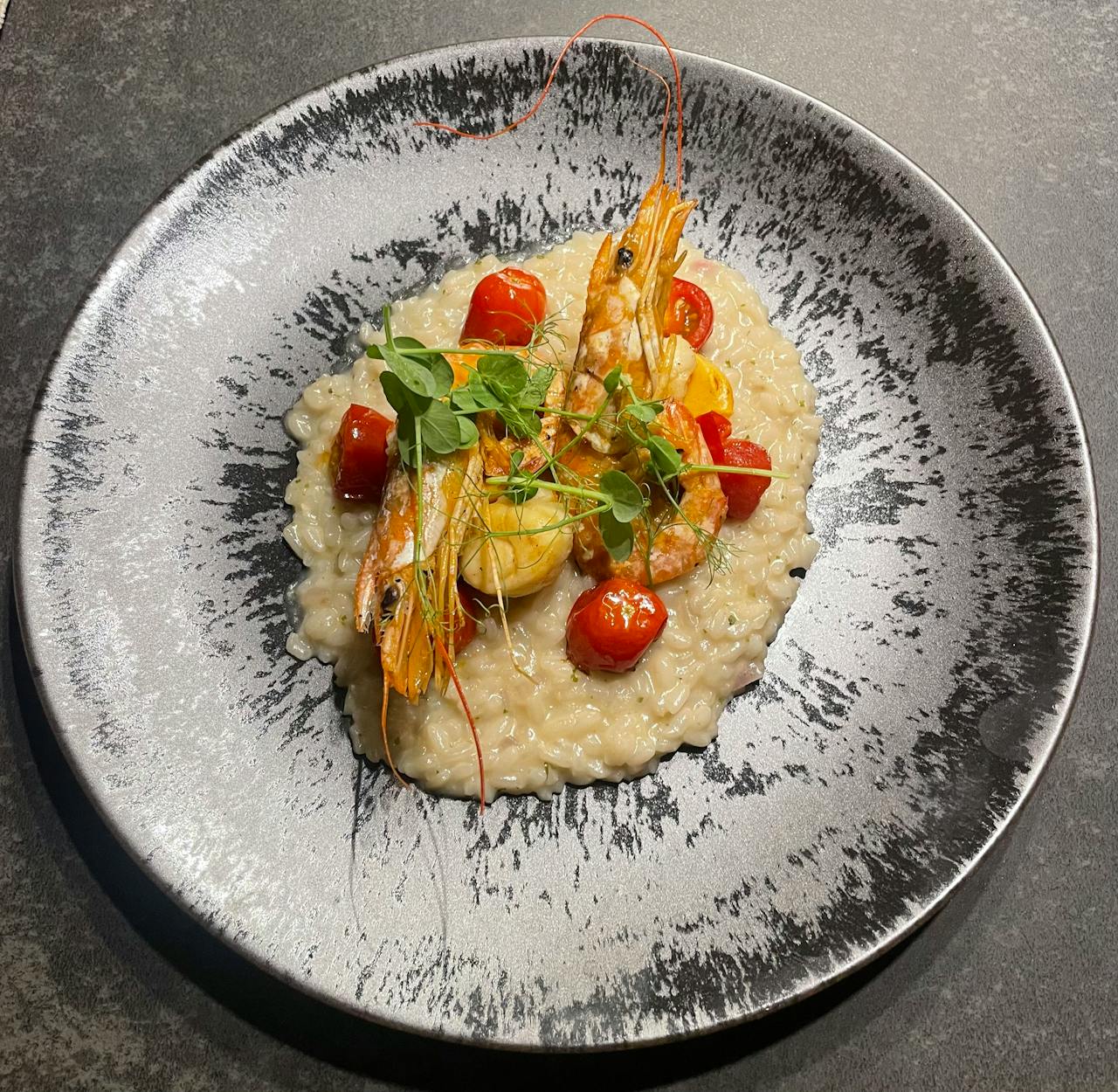 Delicious seafood risotto topped with fresh shrimp and tomatoes, beautifully presented on a designer plate.