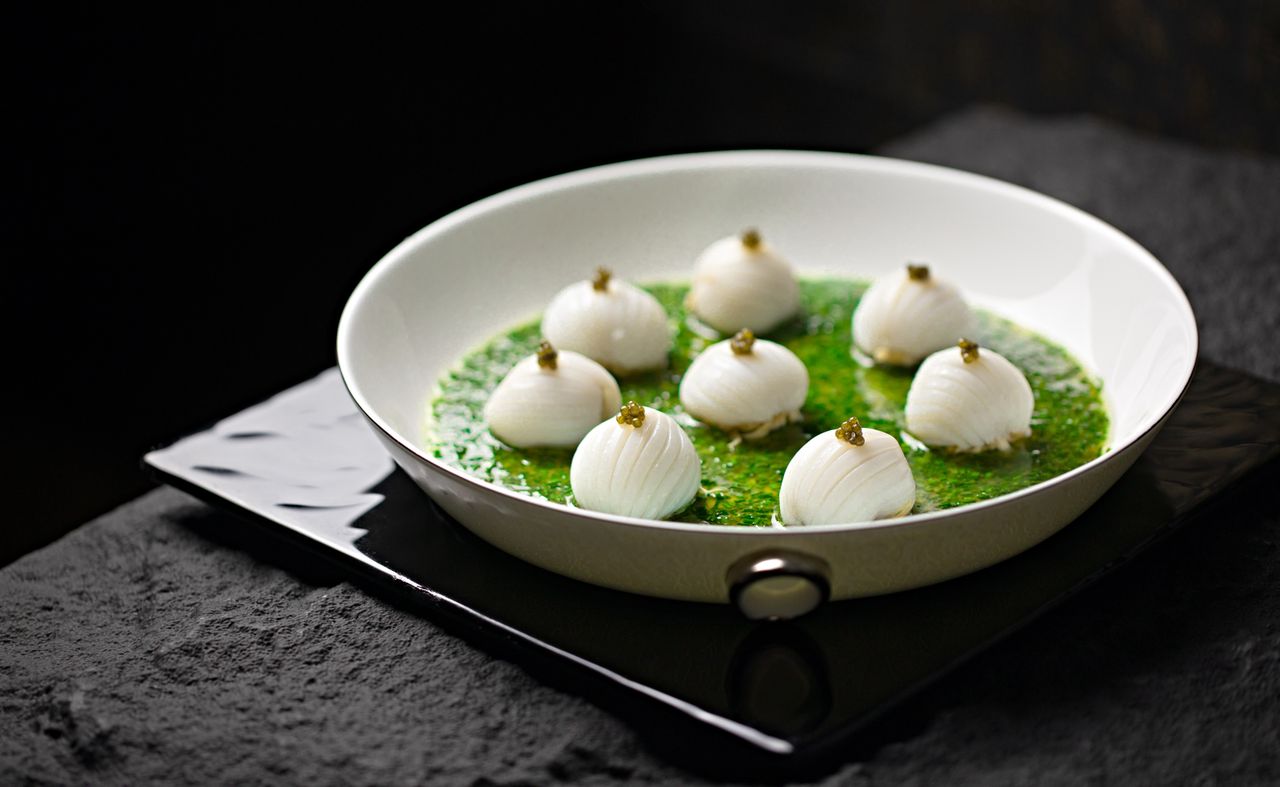 who-we-are-img A gourmet dish featuring onions with green sauce in a stylish white bowl, perfect for food photography.