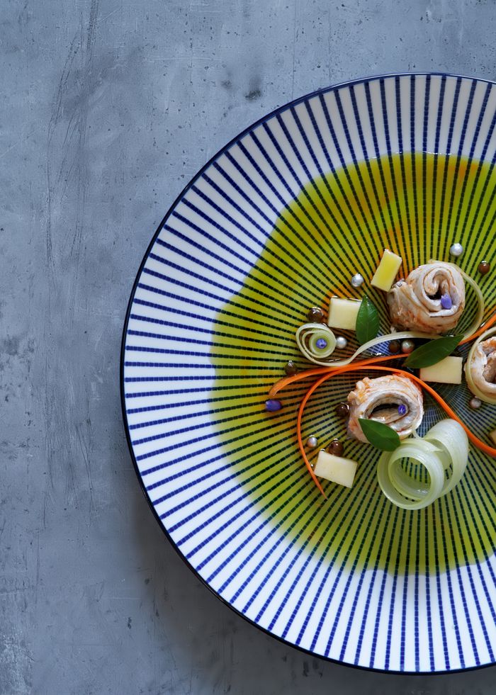 experience-img Elegant gourmet dish with fish and vegetables on a striped plate, top view.