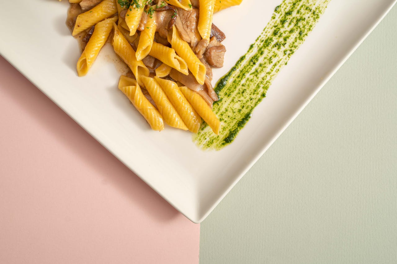 our-journey-01 Appetizing pasta served with mushrooms and a stylish pesto drizzle on a minimalistic plate.